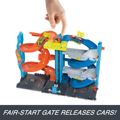 Hand presses a yellow release gate on a multi-level Hot Wheels track set, launching toy cars