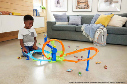 Smiling boy playing with a colorful toy car track, featuring a loop and launcher, surrounded by scattered toy cars on a living room floor