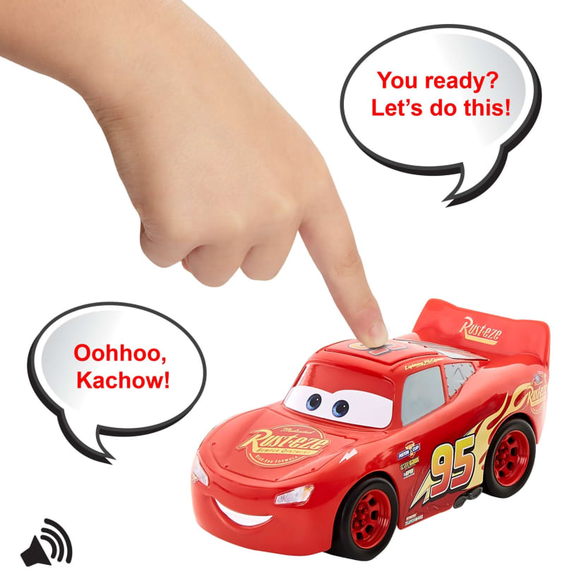 A child's hand presses a button on a red Lightning McQueen toy car, making it speak "Oohhoo, Kachow!"