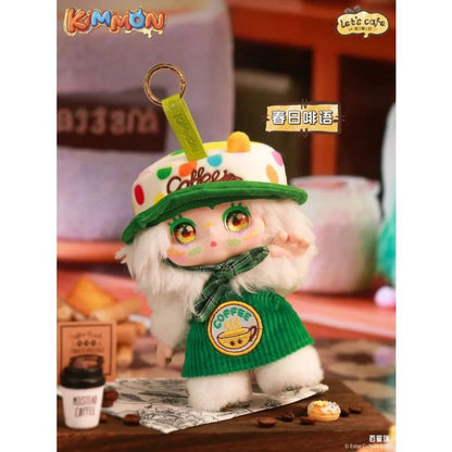 Kimmon plush doll keychain in a green coffee sweater and spotted cap, standing next to tiny coffee props