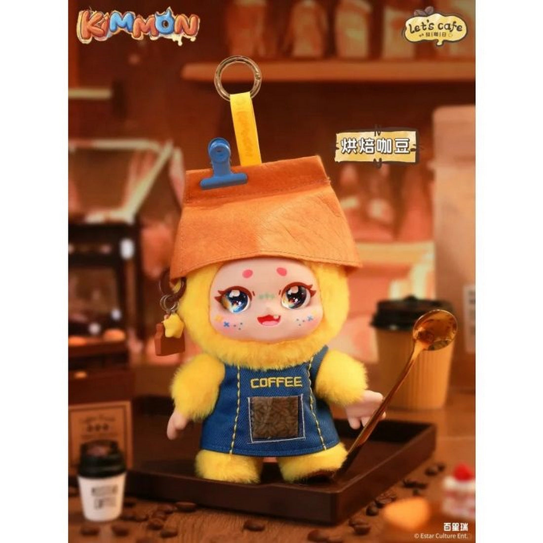 Fluffy Kimmon figure dressed as a barista, wearing a coffee bean bag hat and blue apron in a cafe setting