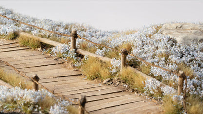 Detailed miniature wooden path with rustic wire fencing, surrounded by dense white flowers and dry grass