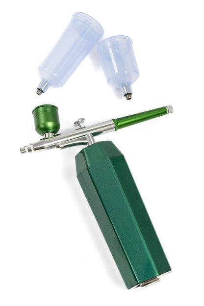 Green handheld airbrush kit with compressor unit and two detached clear paint cups