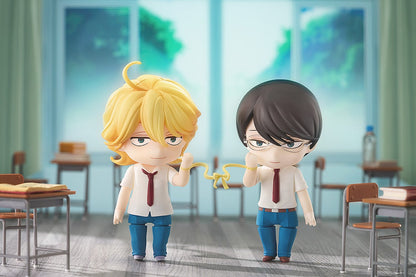 Two blonde and dark-haired anime figures in school uniforms, joined by a yellow ribbon between their wrists in a classroom