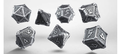 Seven metallic silver polyhedral dice with intricate engraved geometric and runic patterns appear to float against a light grey background