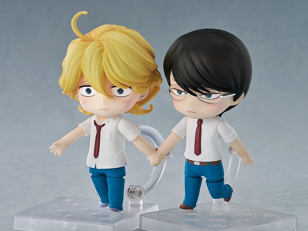 Two anime figures, a blushing blond one and a bespectacled dark-haired one, are holding hands
