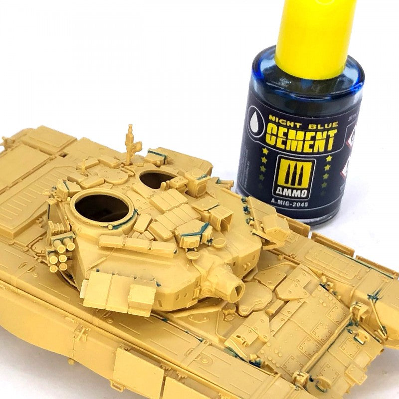 A tan plastic model tank, recently assembled with glue residue, next to a blue bottle of model cement