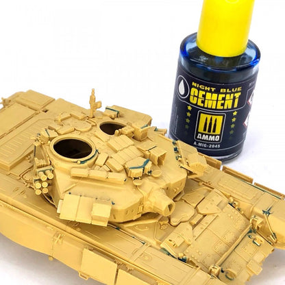 A tan plastic model tank, recently assembled with glue residue, next to a blue bottle of model cement