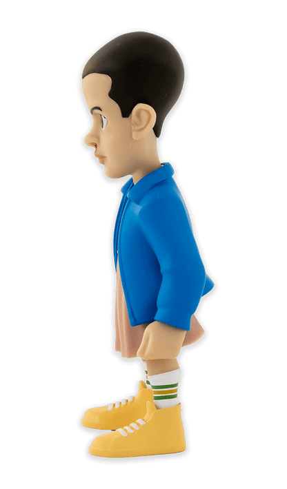 Side view of Minix Stranger Things Eleven collectible vinyl figure with blue jacket pink dress and nosebleed wearing striped socks and yellow shoes