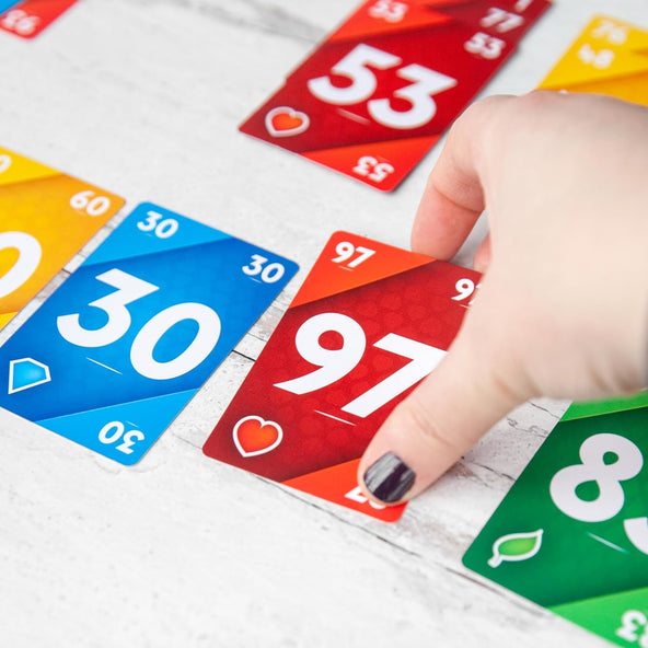 Hand selecting a red 97 card from a spread of Line-it game cards including blue 30 yellow 60 and green 8
