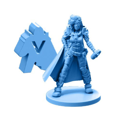 A light blue tabletop miniature of an armored female character holding a cylindrical object, standing next to a gaming token with a V symbol