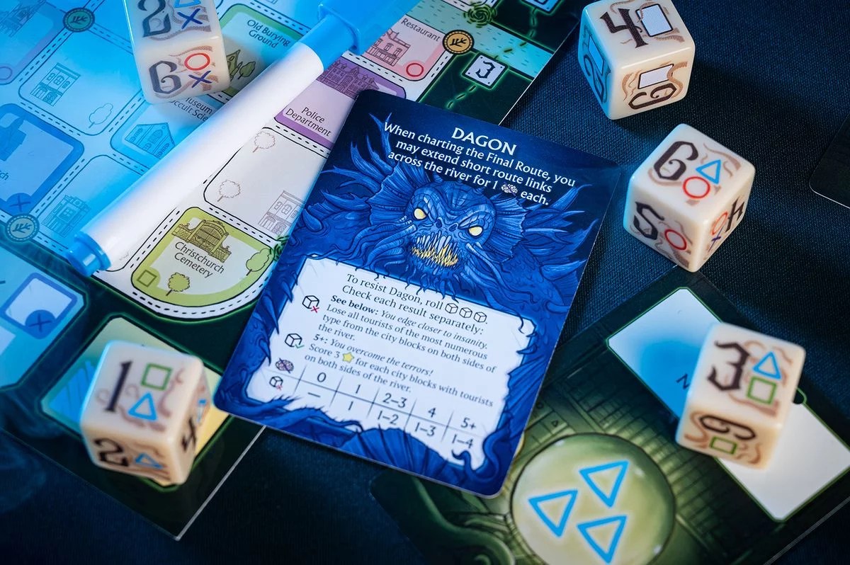 Blue Dagon monster card, custom numbered dice, and a game map section with a dry-erase marker for a horror roll-and-write board game