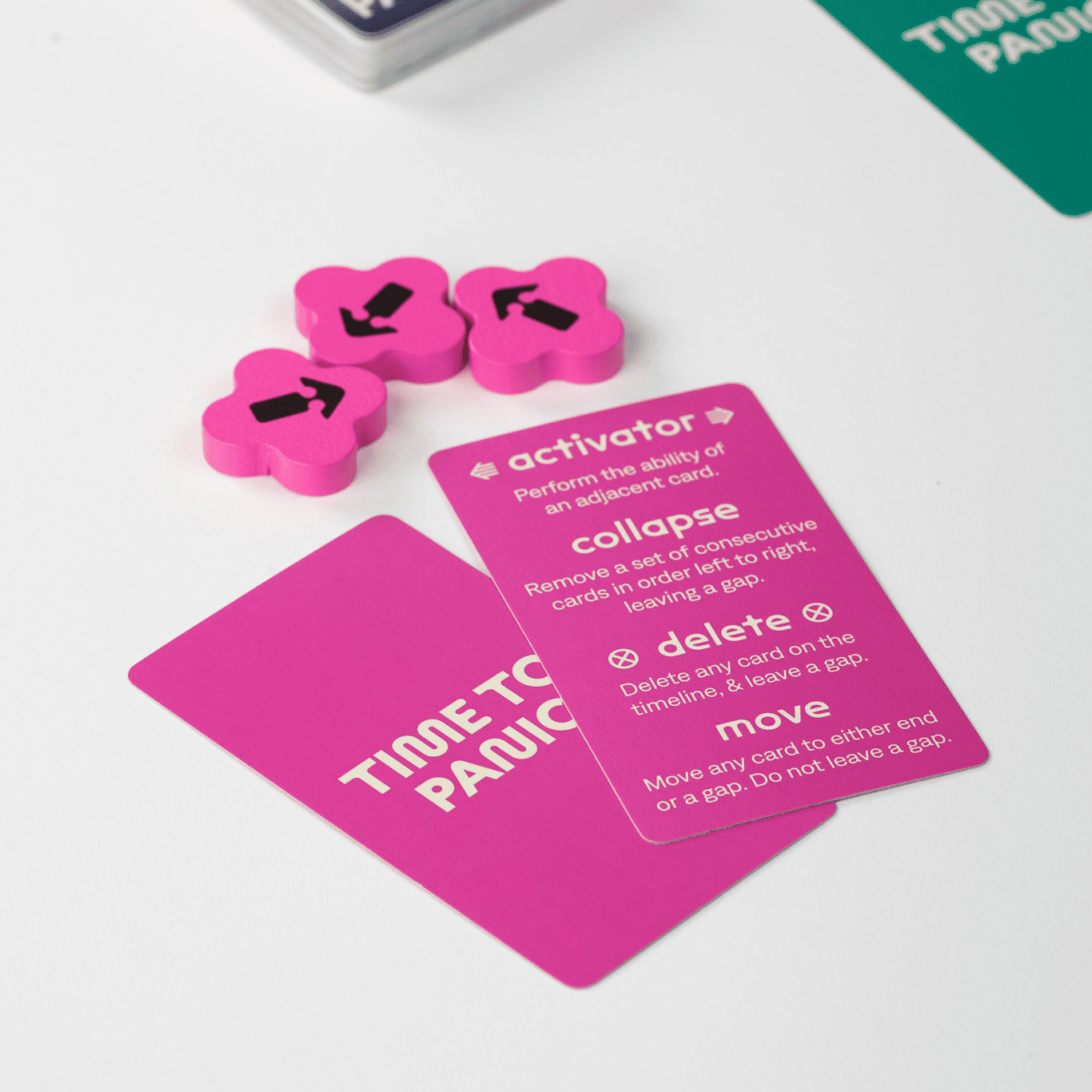 A close-up of pink game cards (one showing rules) and three clover-shaped magenta tokens with arrows on a white table