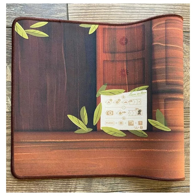 A desk mat with a brown wood grain background, scattered green leaves and a white &quot;Leave No Trace&quot; note