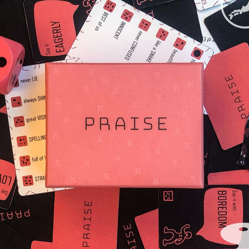 A coral Praise game box is centered, surrounded by scattered black and white game cards featuring text like EAGERLY, INNOCENT, and a coral die