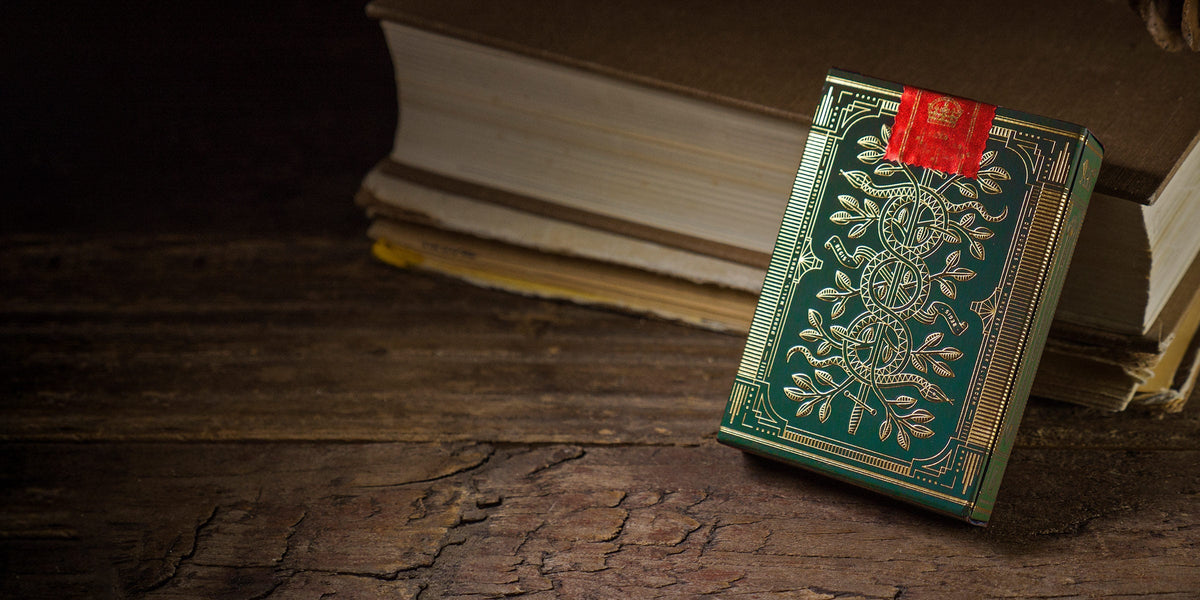 Green and gold ornate playing card deck with a red seal on a dark wooden table, blurred books behind it