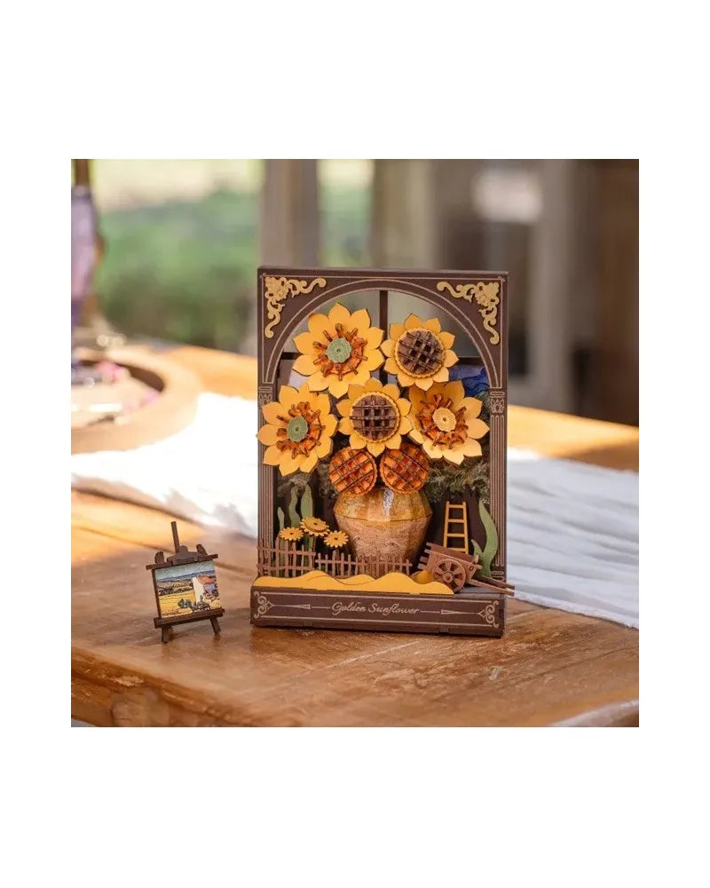 Miniature 3D wooden craft kit showing sunflowers in a framed window, with a tiny painting on an easel