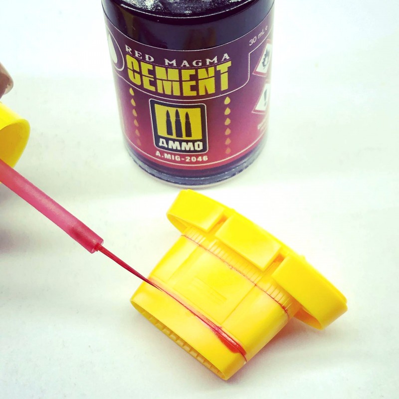 A thin brush applies red model cement from an AMMO bottle onto a yellow plastic part