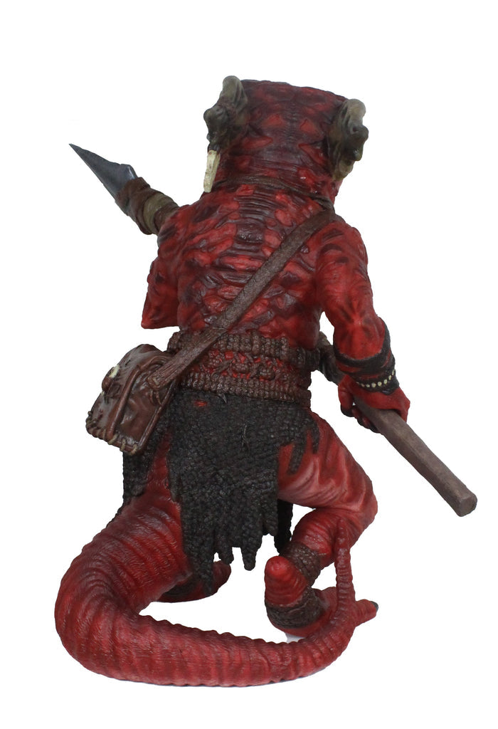A red, scaly, horned kobold figure with a long tail, viewed from behind. It carries a shoulder bag, a staff, and a dagger
