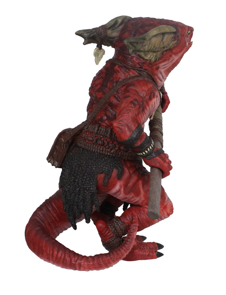 Red reptilian kobold figure with horns and tail, wearing dark armor, stands holding a wooden staff