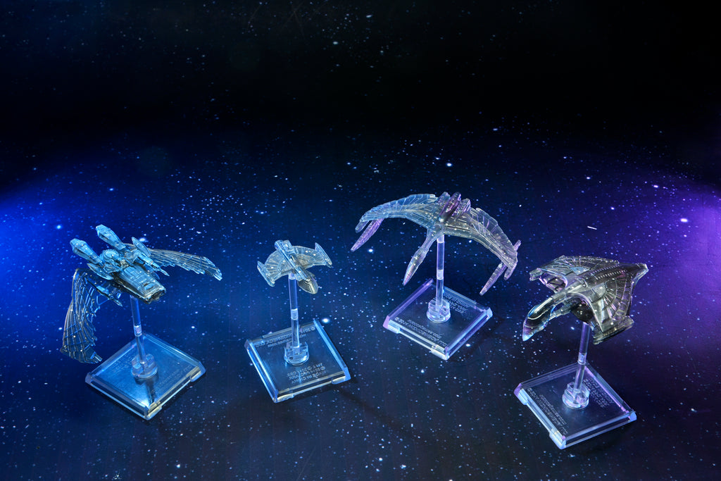 Four detailed, translucent spaceship miniatures glow under blue and purple light against a starry space background