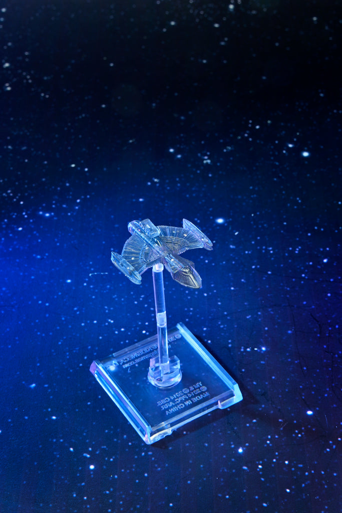 A translucent spaceship model with angled wings sits on a clear stand, against a starry dark blue background