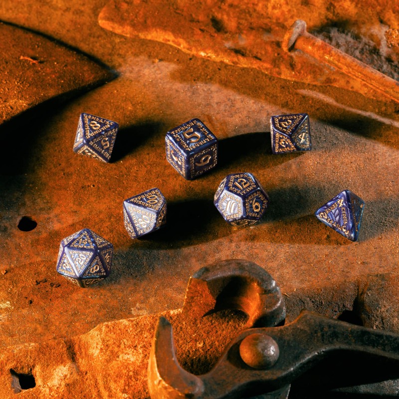 Seven ornate dark blue and gold polyhedral dice scattered on a rusty metal surface next to old tools