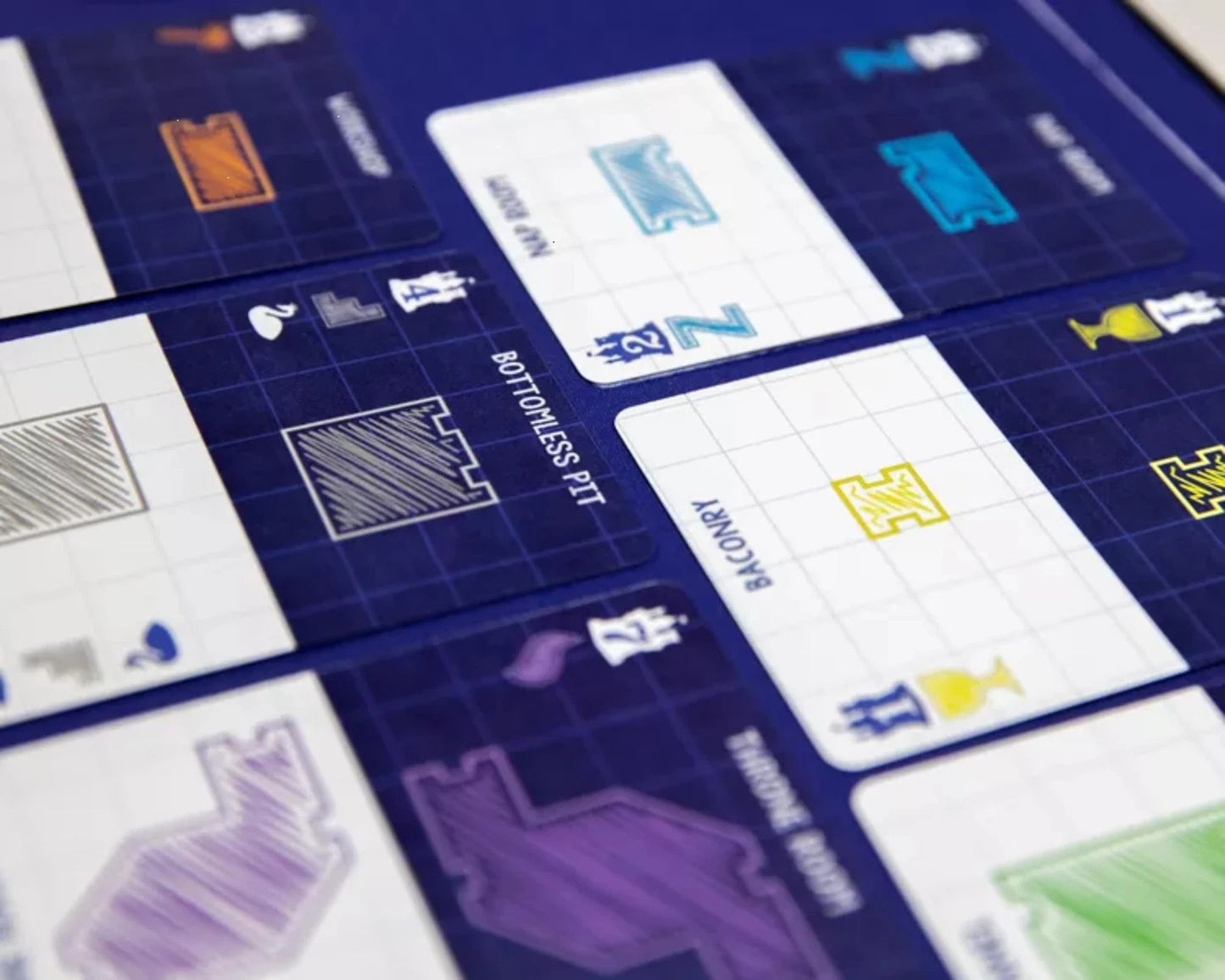 Close-up of game cards showing colorful stylized room designs like 'Bottomless Pit' on a blue grid