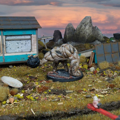 Hulking horror miniature holding a black orb in a derelict diorama with a blue shack and rocky backdrop at sunset
