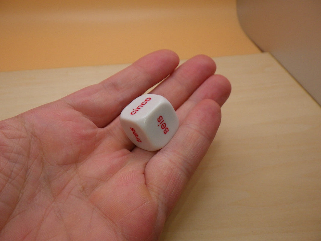 Hand holding a white, six-sided die with red Spanish words 