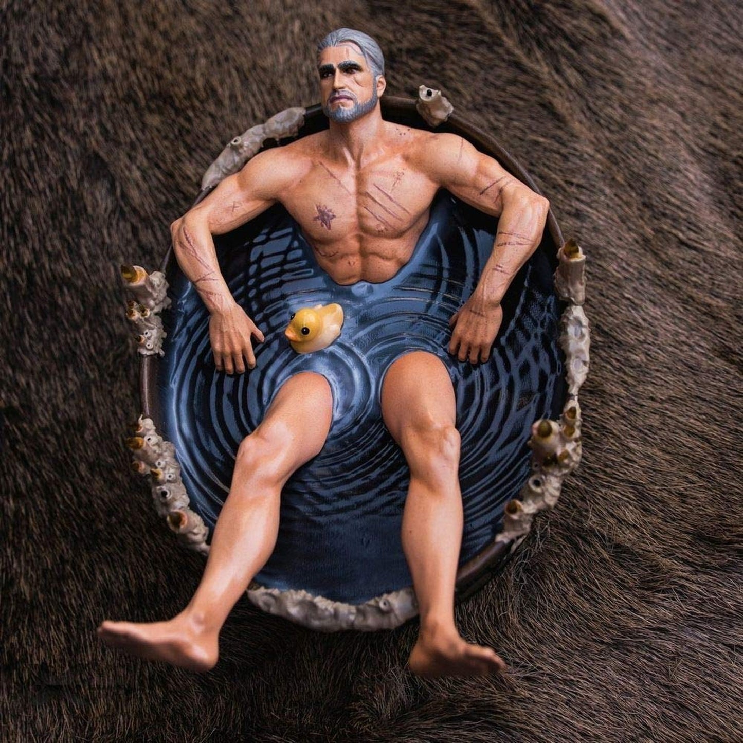 Scarred, muscular Geralt of Rivia action figure with gray hair sitting in a dark bath with a rubber ducky, resting on a brown fur rug