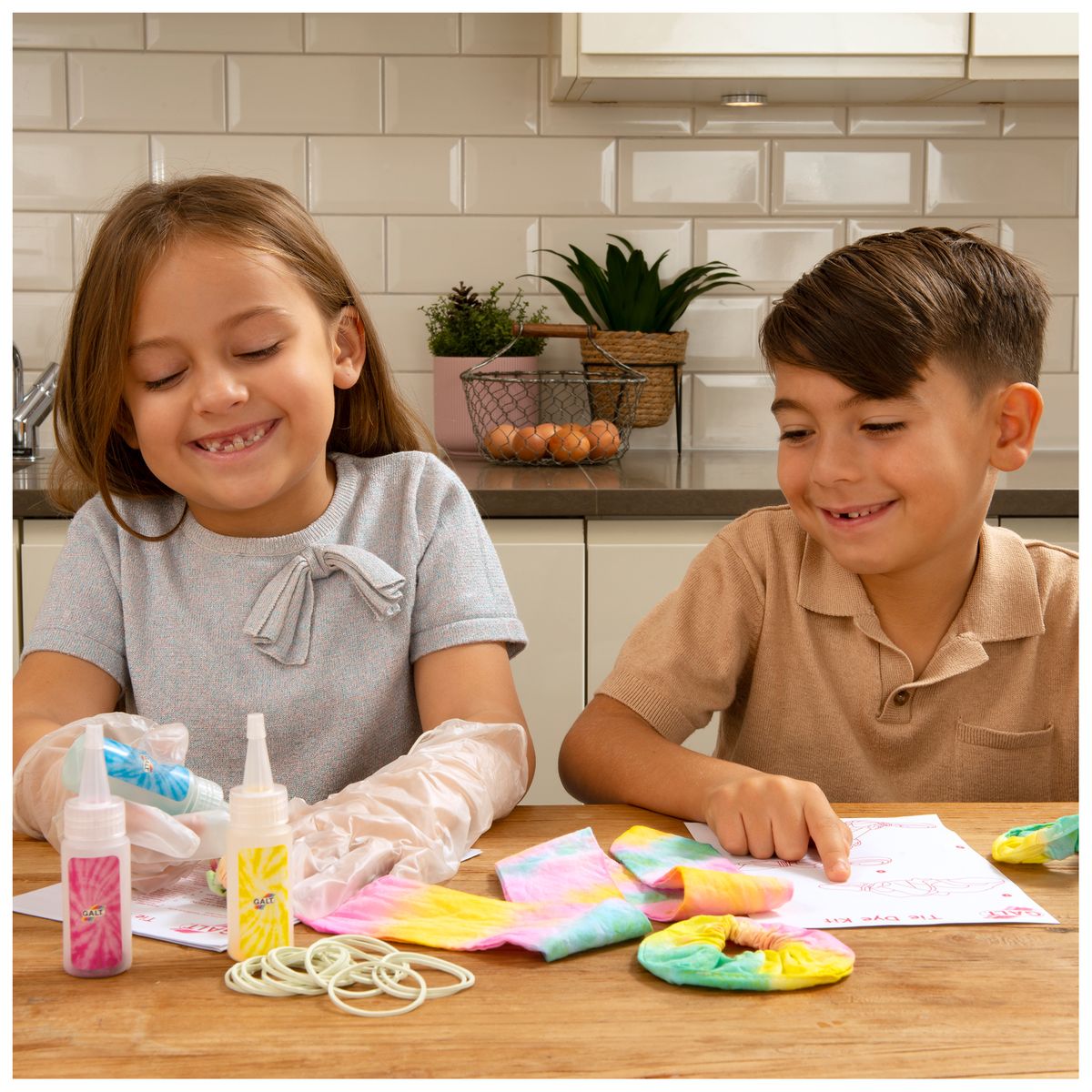 Happy children making tie-dye crafts; girl applies dye while boy looks at instructions