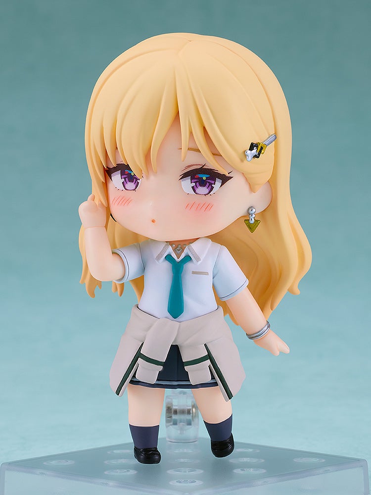 A Nendoroid figure of a blonde girl with purple eyes in a school uniform, sweater tied at waist, blushing, right hand near face