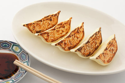Five pan-fried gyoza on a white plate, with a side of soy sauce and chopsticks