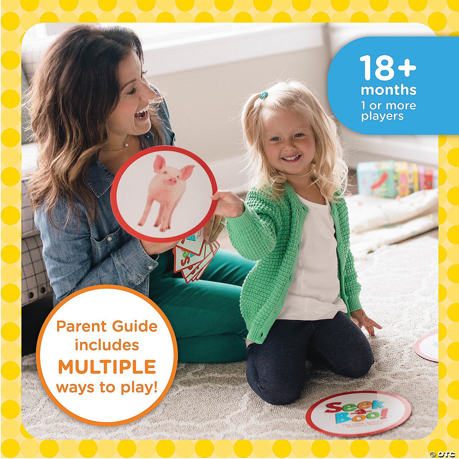 A smiling woman and young child play a card game on the floor. The child holds a pig card