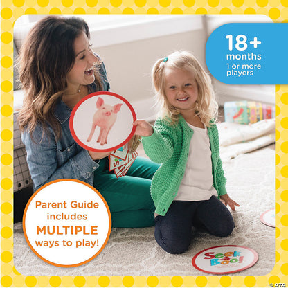 A smiling woman and young child play a card game on the floor. The child holds a pig card