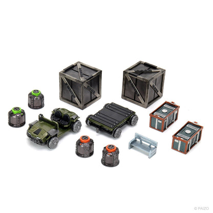 A collection of miniature game terrain: two crates, a green buggy, a flat cart, four canisters, two small buildings, and a bench