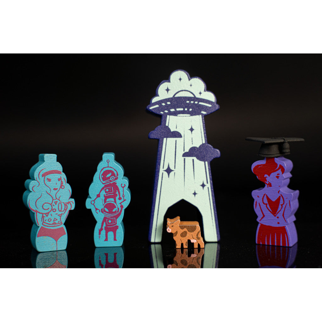Wooden board game pieces: Retro woman, robots, UFO abduction of a cow, and a graduate character token on a black background