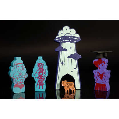 Wooden board game pieces: Retro woman, robots, UFO abduction of a cow, and a graduate character token on a black background