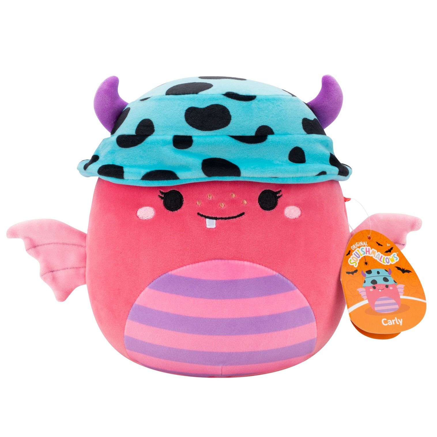 The pink Carly Squishmallow monster plush features purple horns poking through a blue spotted cap, small pink wings, and a striped belly