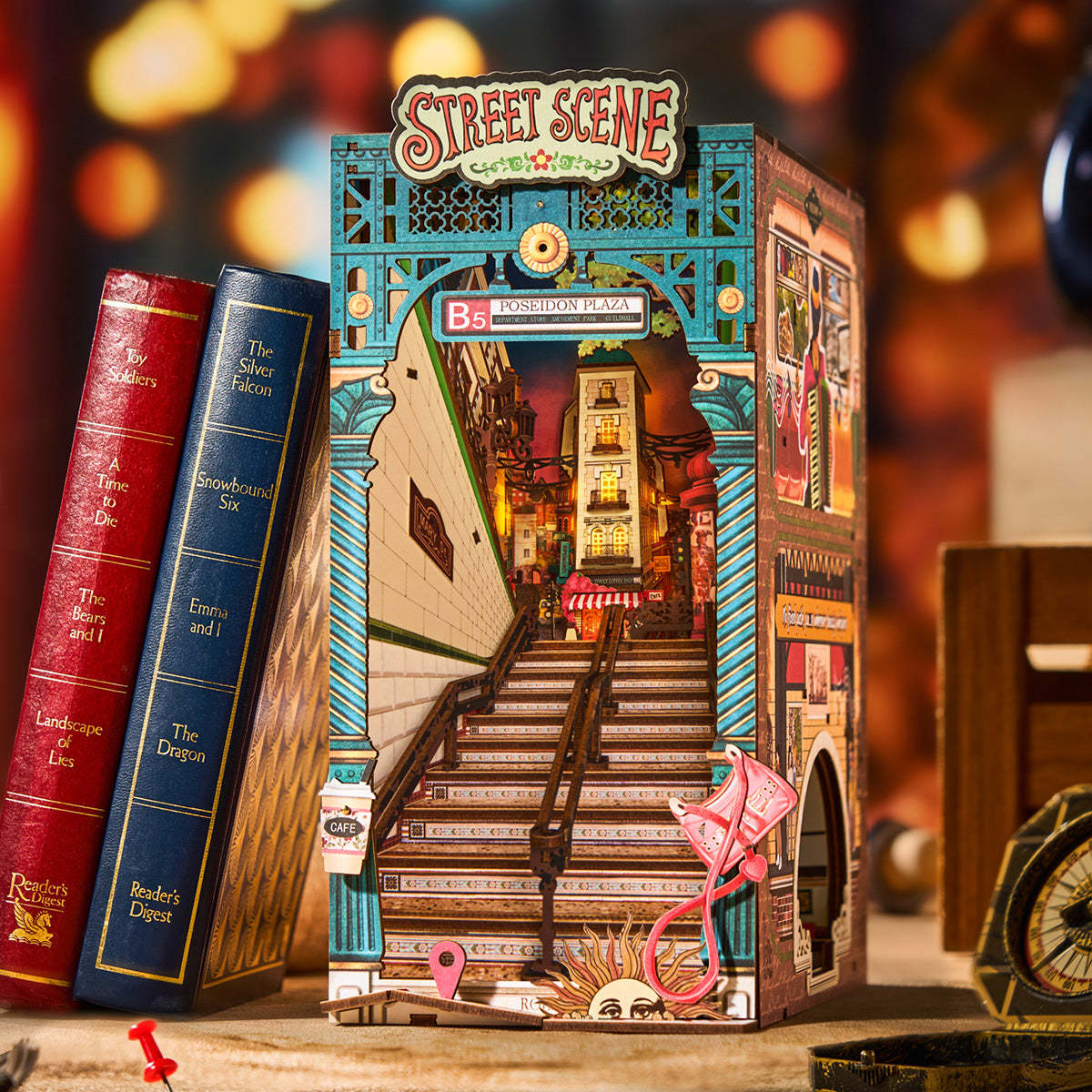 Intricate wooden book nook diorama of a miniature illuminated city street scene with long stairs, next to two books