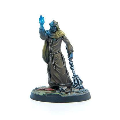 A hooded miniature figure in a brown robe with blue skin raises a glowing blue crystal and holds an ornate staff