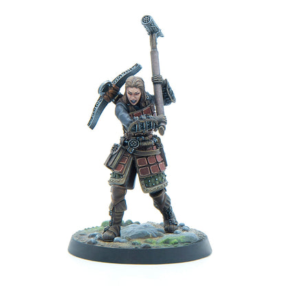 Hand-painted miniature of a fierce dwarven female warrior in armor, raising a hammer with a pickaxe on her back