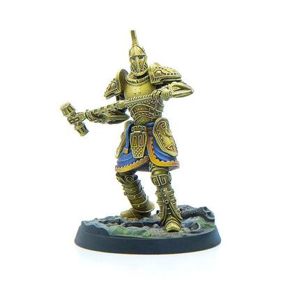 A miniature gold-armored warrior with blue trim, holding a large two-handed hammer