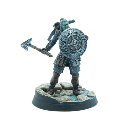 A green-skinned orc warrior miniature with an axe and ornate shield, standing on a rocky base