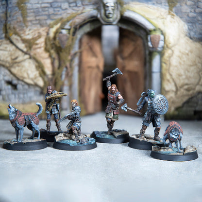 Fantasy miniatures: armored warriors, an orc, and two wolves posed ready for battle before an ancient stone gate