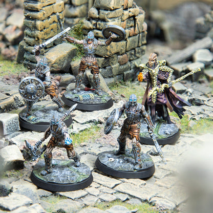 Five fantasy miniatures: four skeletal warriors with glowing eyes and weapons, and a robed sorcerer, on ruined terrain
