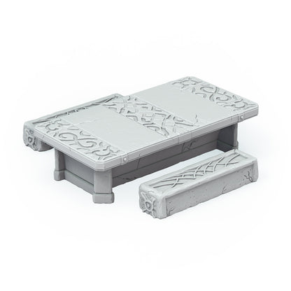 A grey miniature stone table with intricate carvings sits next to a matching stone bench
