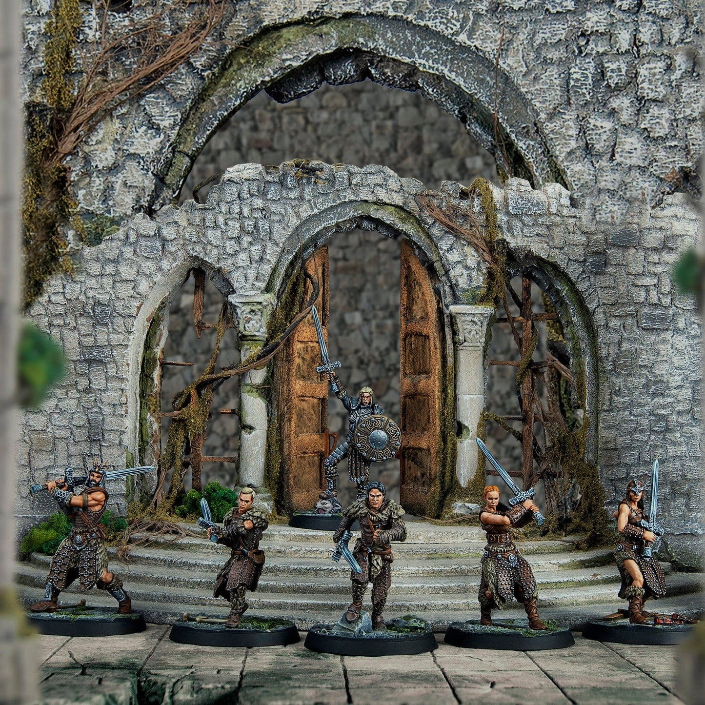 Five armored fantasy warrior miniatures, wielding swords, stand before a mossy stone ruin with an open door.