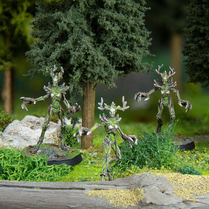 Three humanoid tree-like miniatures with antlers and glowing green accents stand in a miniature forest